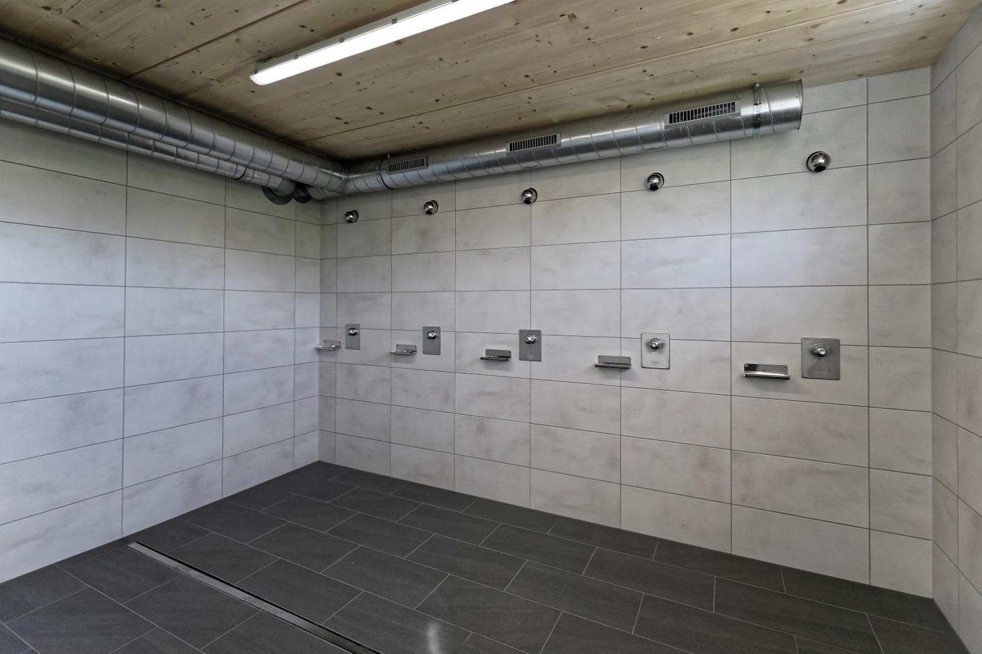 Gefliester Duschraum mit Holzdecke und sichtbaren Rohrleitungen
